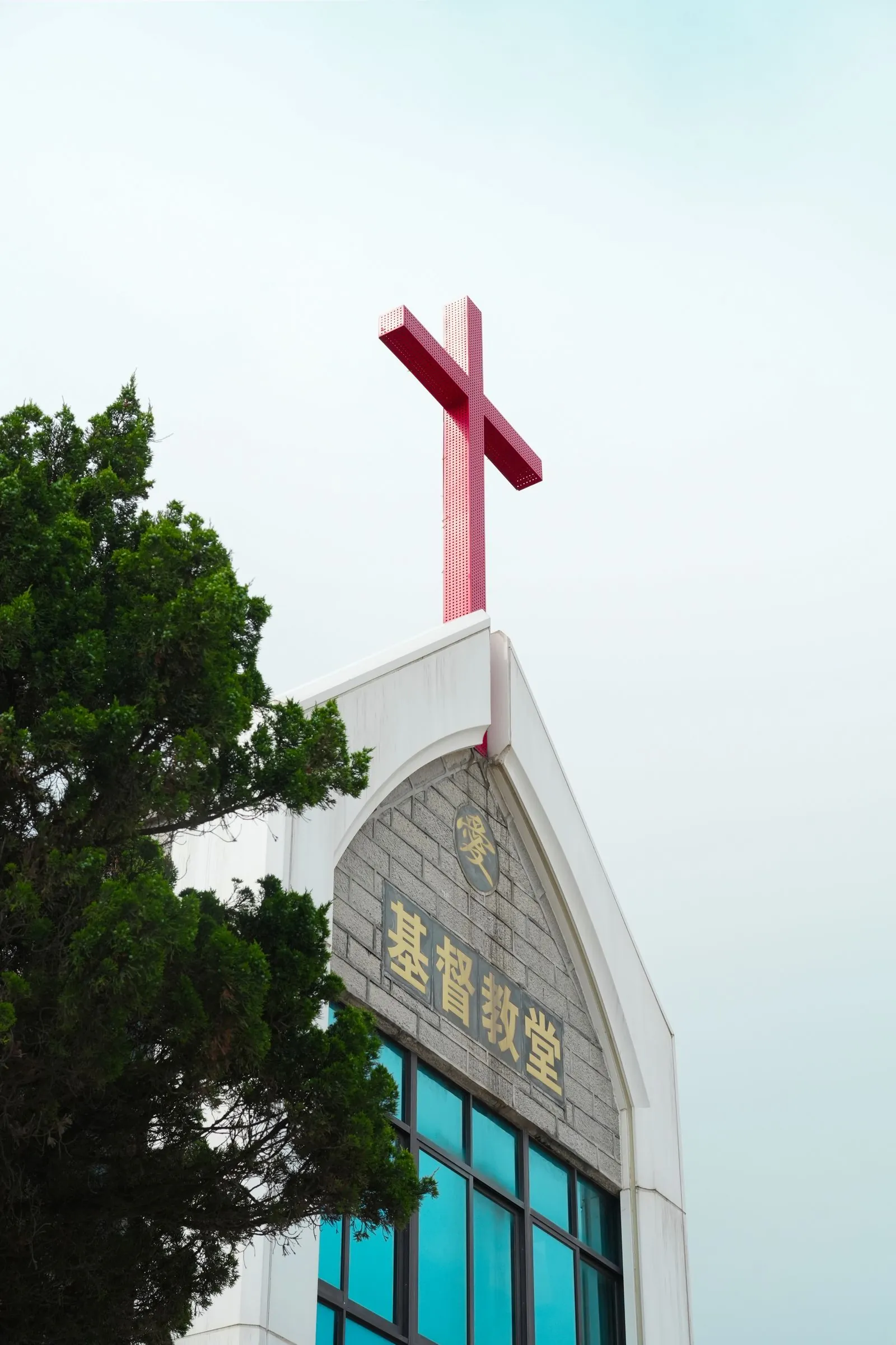 基督教堂外牆與屋頂上的紅色十字架,旁邊有綠樹