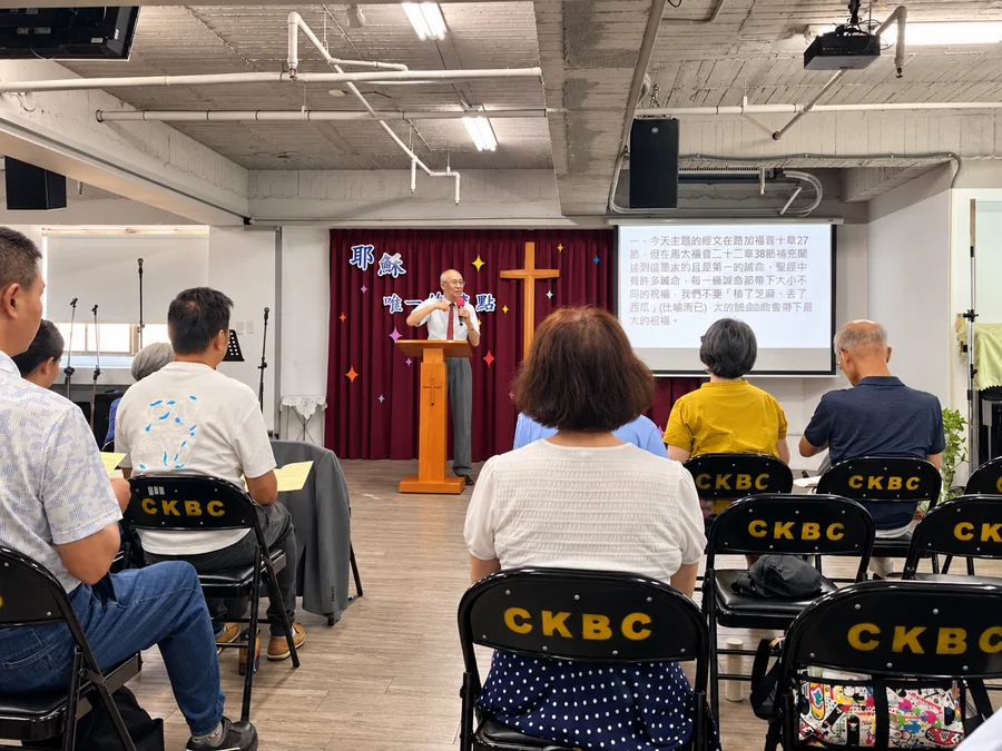 基督國度台中伯特利教會主日聚會現場，講員站在講台前分享，會眾坐在椅子上聆聽